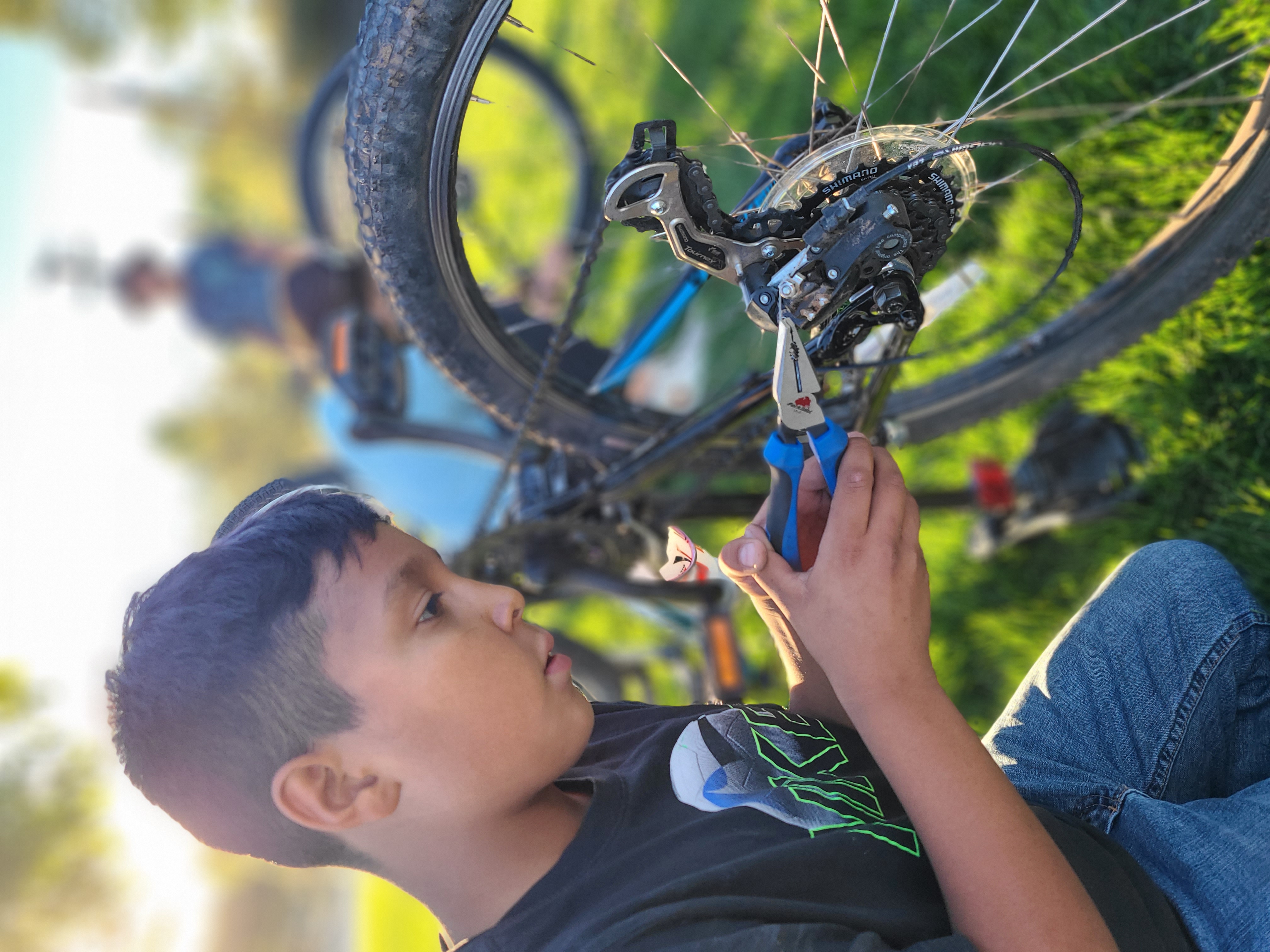 A child works on a bike while holding tools in their hand